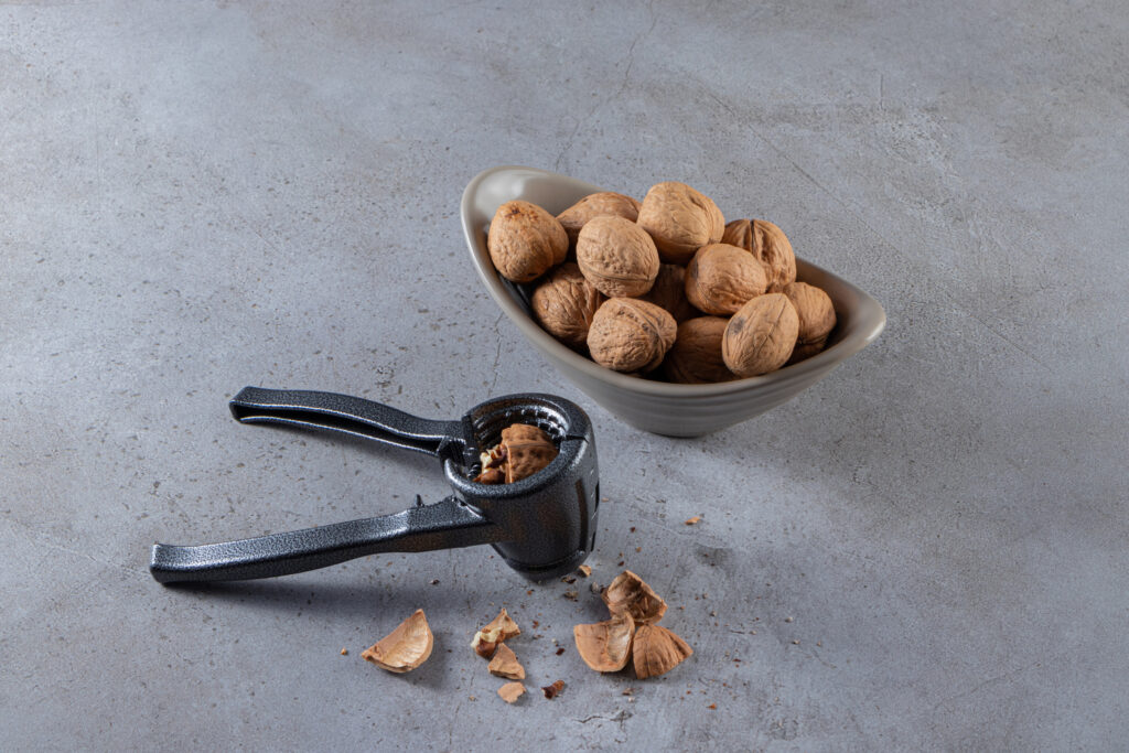 Gray bowl of organic shelled walnuts and nut cracking toll on stone background